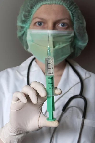 Doctor in mask holding a medical syringe.