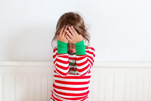 Small girl in pajamas covering her face with her hands
