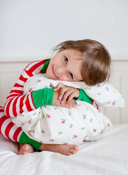 Small girl in striped pajamas sitting on her bed