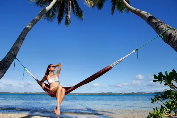 Young woman in bikini sitting in a hammock between palm trees, O