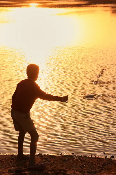 Silhouette of a boy throwing stones in a water, Khichan village,