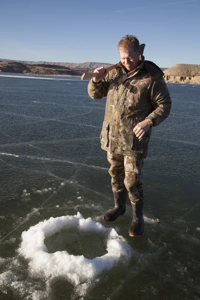 Man in camo chopping hole in ice with axe proud