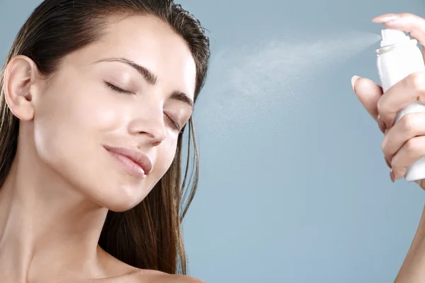 Beautiful woman applying spray  water treatment on face