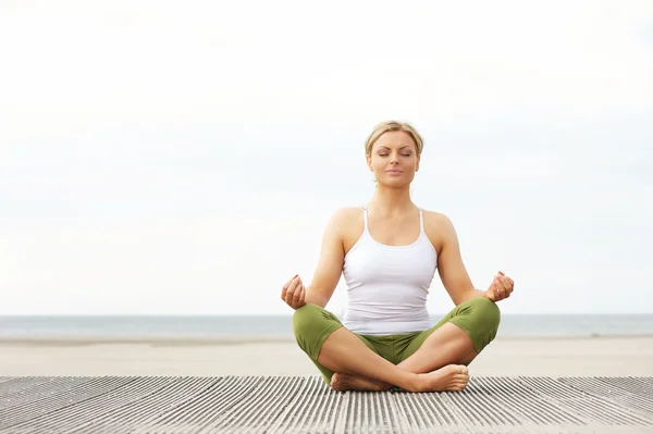 Beautiful young woman sitting in yoga pose at the beach