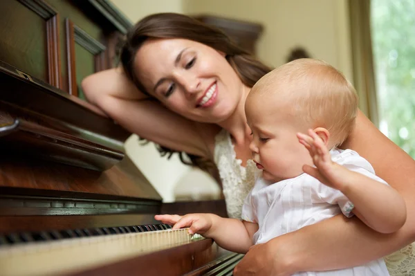 Happy mother smiling as baby plays piano
