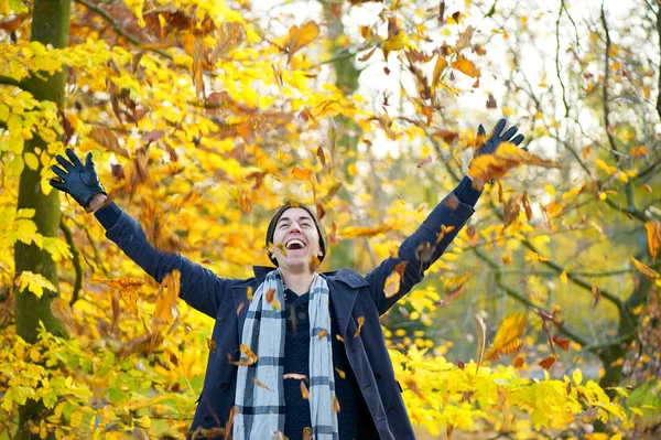 Happy smiling man throwing leaves with open arms in autumn