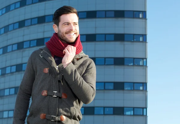 Young man with beard smiling outdoors with jacket and scarf