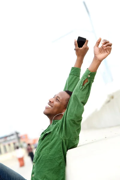 Man smiling with arms raised and mobile phone