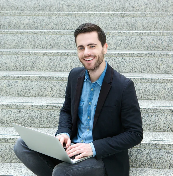Young man sitting on steps and smiling with laptop