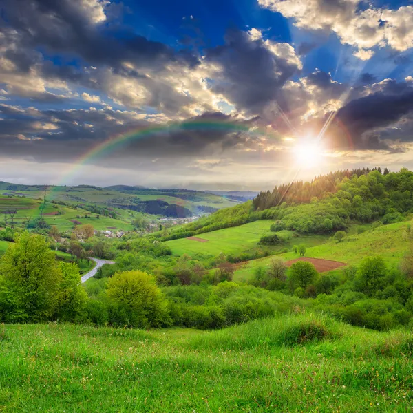 Village on hillside meadow with forest at sunset