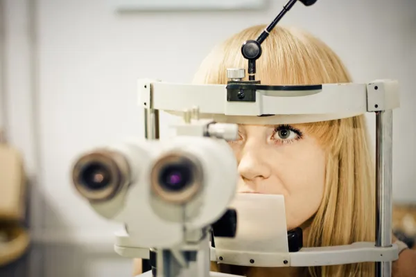 Optometry concept - pretty young woman having her eyes examined by an eye doctor on a slit lamp