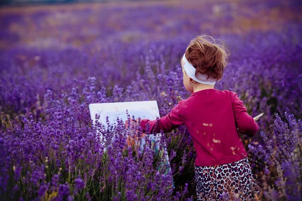 The little girl draws a picture in a lavandovy field