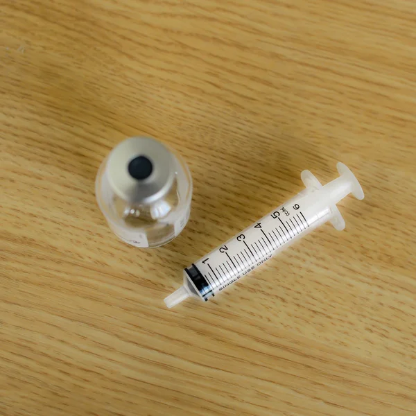 Medicine vials and syringe on wooden table