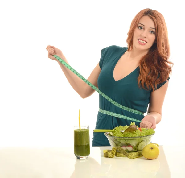 Woman with a centimeter on her waist thinking on dieting while eating organic healthy salad,fruits and smoothie for a perfect body. Green food for a healthy life