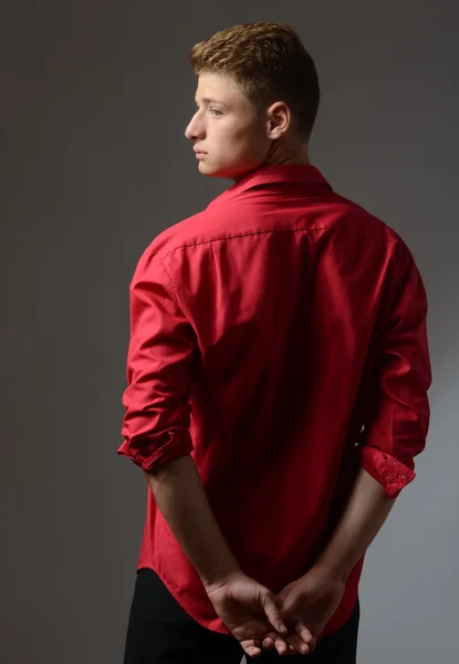Beautiful young man wearing a red shirt posing with his back and looking into the light