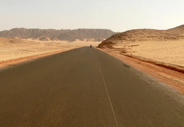 Africa. The road running through the Sahara desert. Unknown man riding a motorcycle on the road.