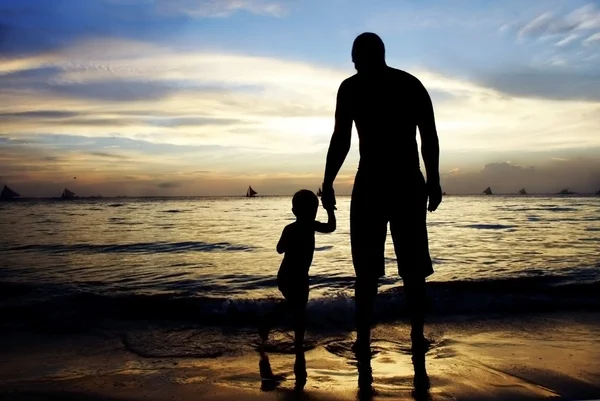 Father and son on sunset sea and sky background