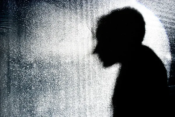 Person\'s silhouette behind textured glass wall