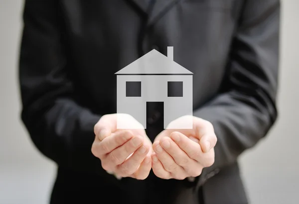 The hands of a man holding a house - insurance and protection concept