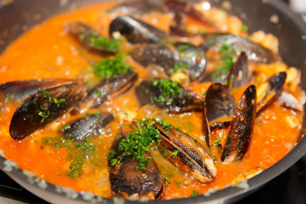 Mussels being fried in pan with tomato sauce and herbs