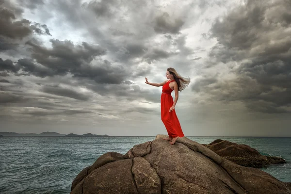 Woman in red dress stands on a cliff with a beautiful sea view a