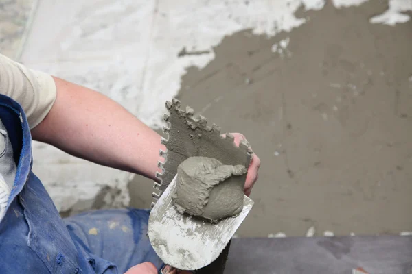 Construction worker is tiling at home tile floor adhesive