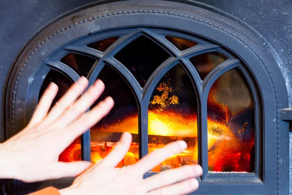 Woman warming her hands at fire fireplace interior. Heating.