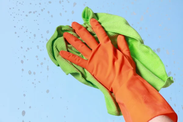 Gloved hand cleaning window with rag