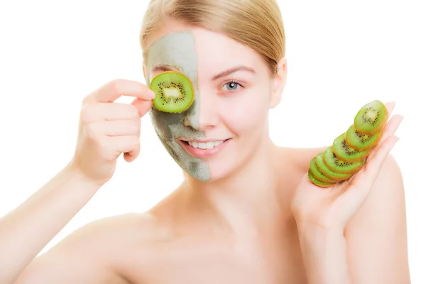 Woman in clay mask on face covering eye with kiwi