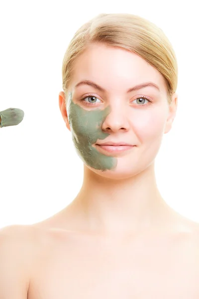 Woman applying clay mud mask on face.