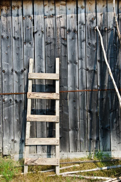 Old wood ladder leaning over a grey wooden wall.