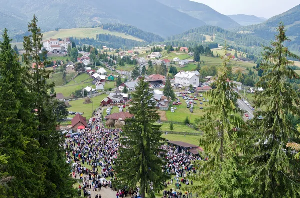 Gathering of many people on a green lawn watching and listening to a religious ceremony happening on the stage.