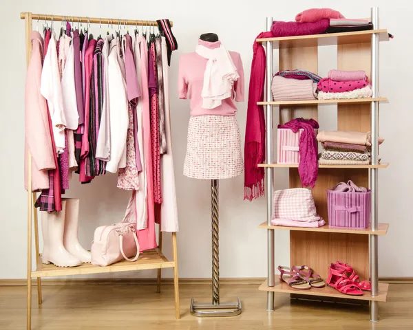 Dressing closet with pink clothes arranged on hangers and shelf, outfit on a mannequin.