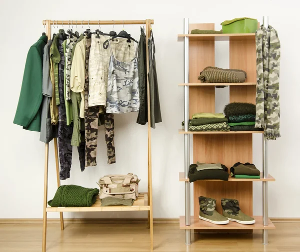Dressing closet with military camouflage khaki green clothes arranged on hangers and shelf.