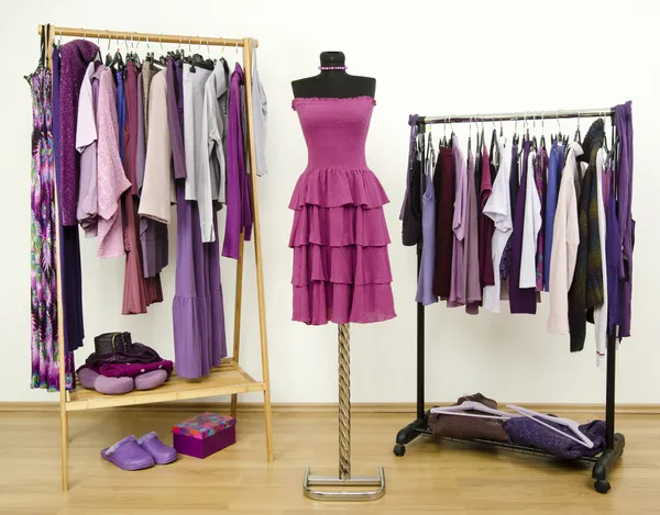 Wardrobe with purple clothes arranged on hangers and a dress on a mannequin.