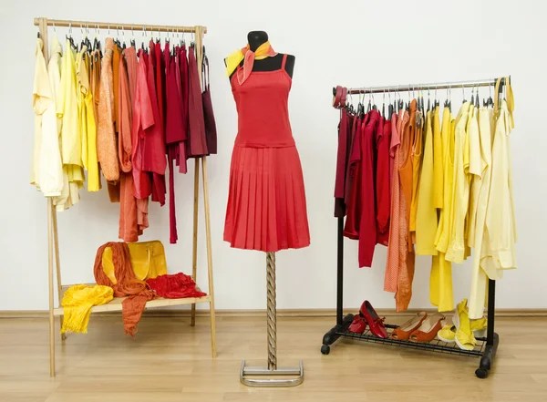 Wardrobe with yellow, orange and red clothes arranged on hangers and a red outfit on a mannequin.