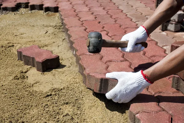 A worker laying red concrete paving blocks.