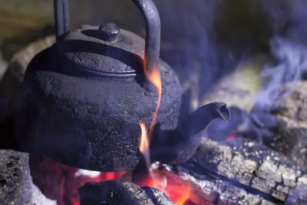 Old kettle on the fire at an outdoor campsite.