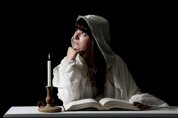 Young woman in white reading with candle light at night