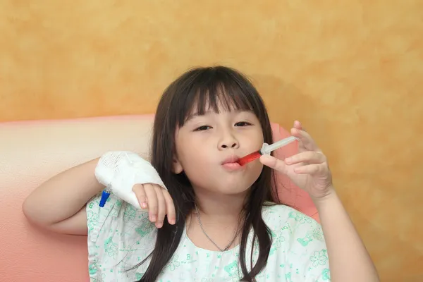 Little girl drinking syrup with syringe.