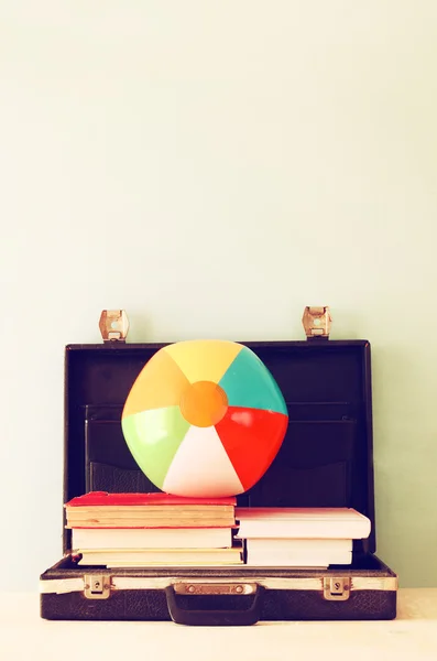 Open briefcase with books and beach ball. sea in the background, filtered image.