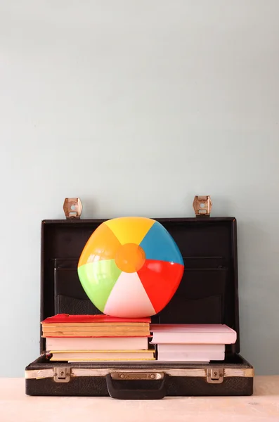 Open briefcase with books and beach ball. sea in the background, filtered image.