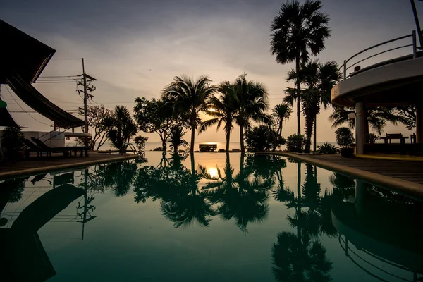 Dawn at early morning over peaceful still swimming pool with palm silhouettes in summer resort in thailand
