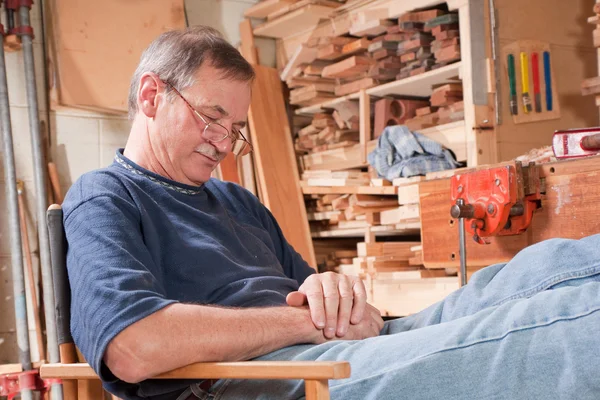 Elderly man asleep in chair in workshop