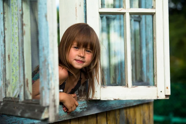 Beautiful little girl looks out the window rural house