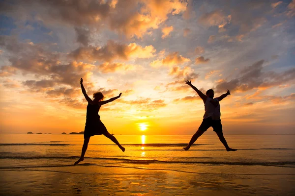 Young couple in a jump on the sea beach at sunset