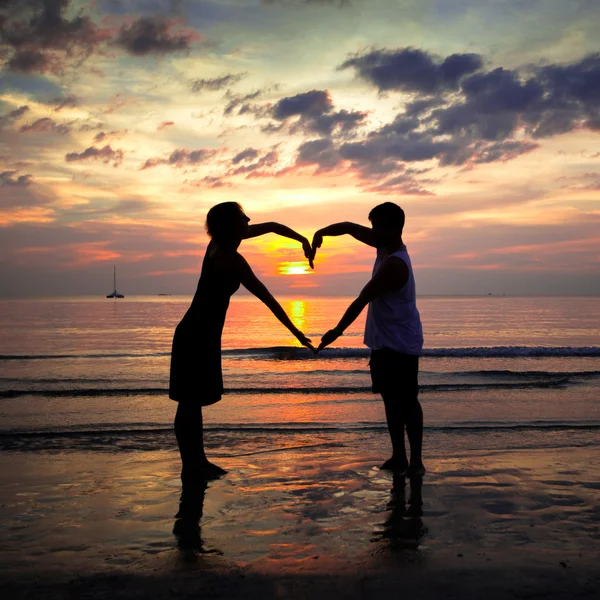 Young couple holding hands heart-shaped on the sea beach at sunset