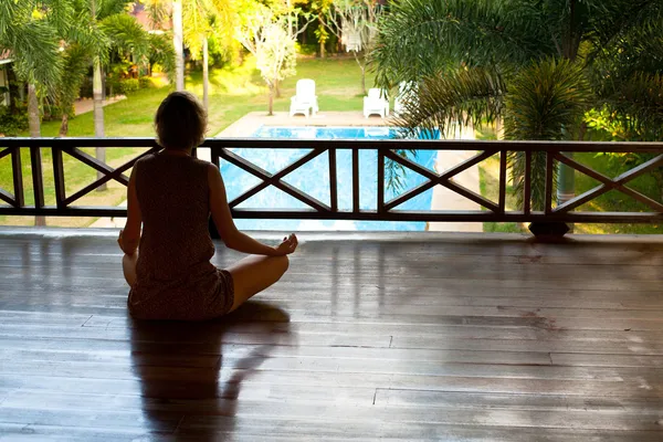 Young woman sitting in lotus position with the balcony looking at the pool in the spa resort