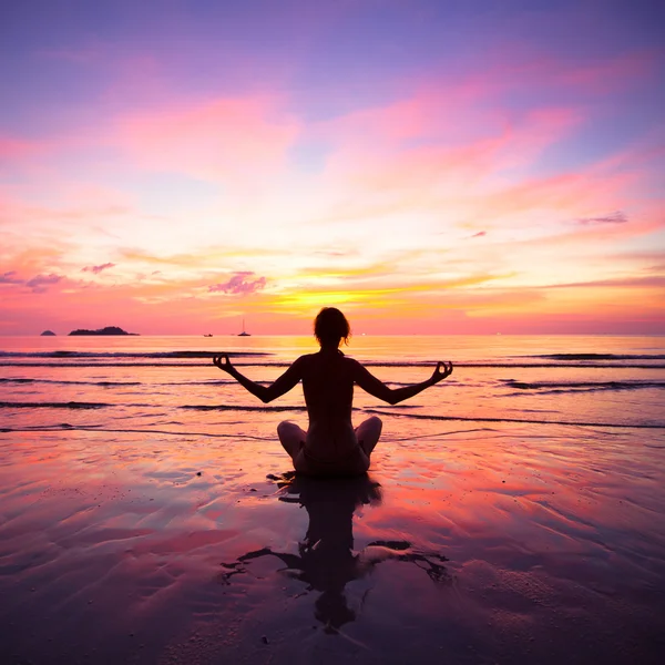 A woman practicing yoga sitting on the beach during sunset