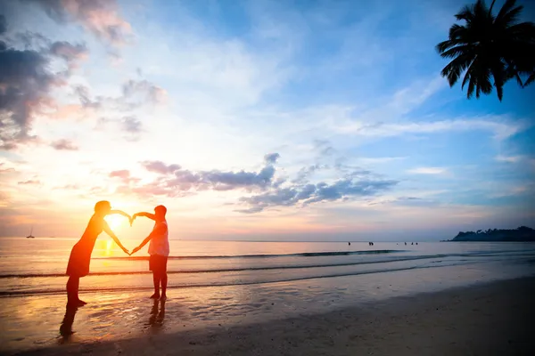 Young couple holding hands heart-shaped on the sea beach at sunset.